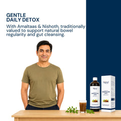 A man in an olive green t-shirt stands behind a wooden table displaying a bottle and box of Triphal Digesto Care Juice alongside a glass of the dark liquid and green leaves. The left side has text reading 'GENTLE DAILY DETOX' on a split white and dark navy background.